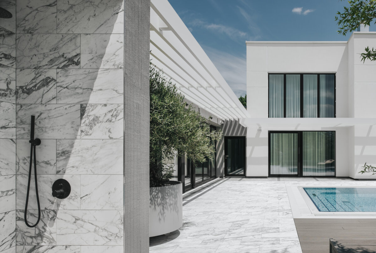 A large building with large windows, a terrace,an olive tree,and a pool.