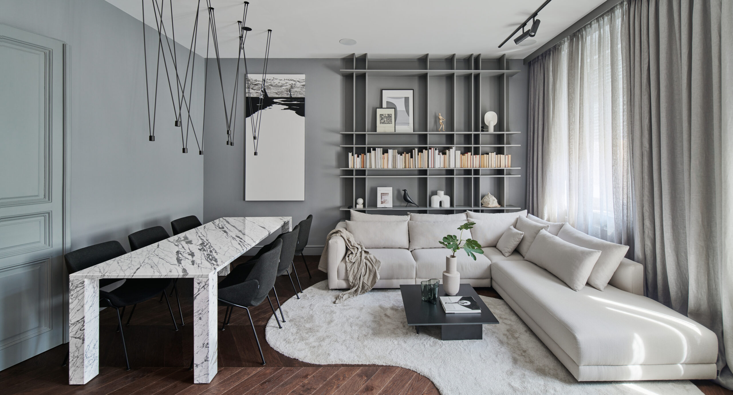 A living room with a couch, a coffee table, a large bookshelf, a table, a chairs, and a window.